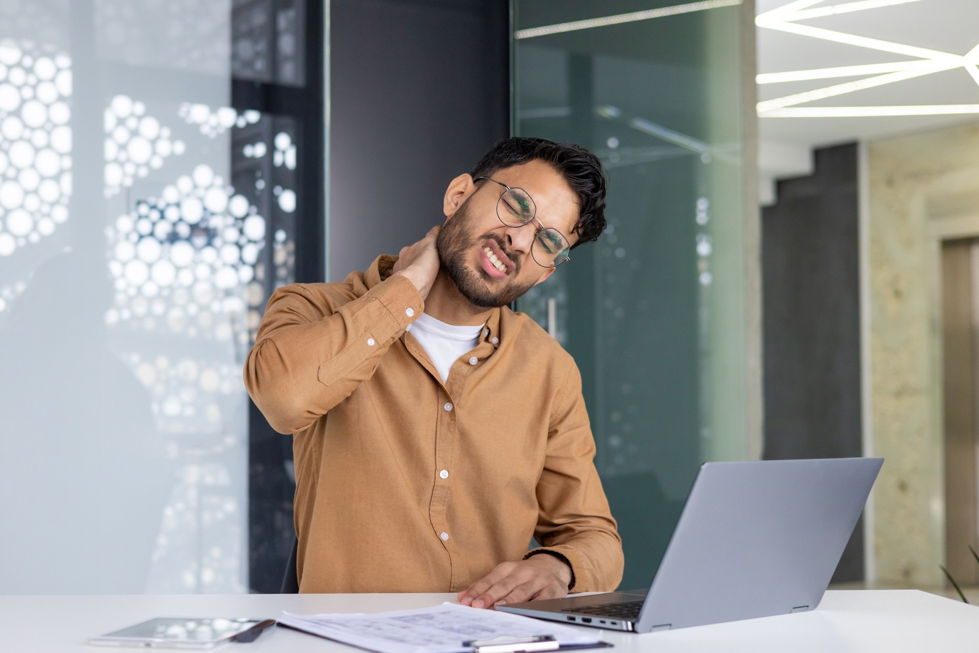 Office worker experiencing neck pain while working on laptop at desk